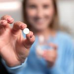 Young-Woman-Hand-Holding-White-Pill-Smiling-1200x800