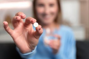 Young-Woman-Hand-Holding-White-Pill-Smiling-1200x800